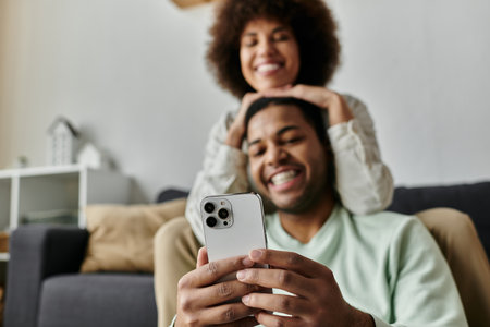 Cheerful African American woman sitting near her husband with hearing aid and looking at phone.の写真素材