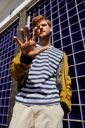 Red-haired man in debonair attire with hand in front o face in city setting.