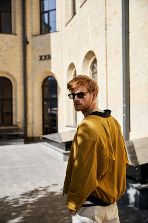 Young red-haired man in yellow jacket and white pants strolling through city streets.の写真素材