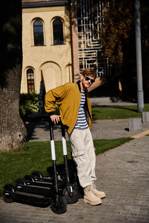 Young red-haired man in debonair attire standing beside scooters in the city.