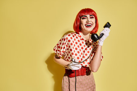 A stylish redhead woman with pop art makeup holds a phone against a yellow backdrop.の写真素材