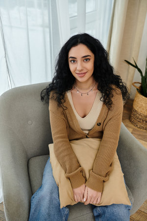 Young woman in casual attire seated with pillow on chair.