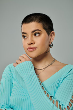 A young woman with short hair poses in stylish casual attire against a gray background.
