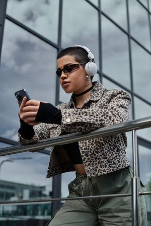 A young woman with short hair and a leopard print jacket listens to music on headphones while...