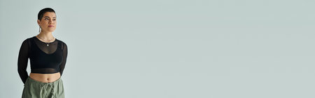 A young woman with short hair standing confidently in stylish casual attire in front of a white wall.の写真素材