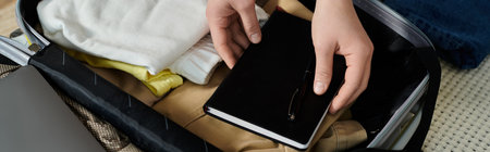 cropped young woman carefully places a book inside a suitcase, preparing for an adventurous...