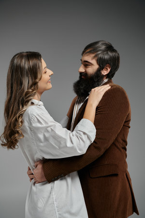A loving couple, dressed in sophisticated attire, embrace each other against a neutral gray backdrop.の写真素材