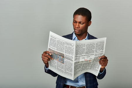 Stylish African American businessman in checkered blazer, fully immersed in reading a classic newspaper.の写真素材