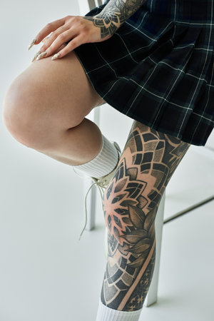 A close-up shot of a young womans tattooed leg in a plaid skirt.の写真素材