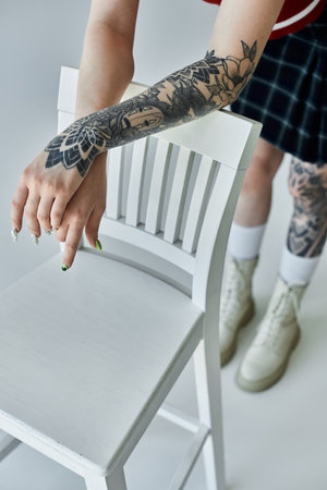 A young woman with tattoos on her arm leans on a white chair. She is wearing a plaid skirtの写真素材