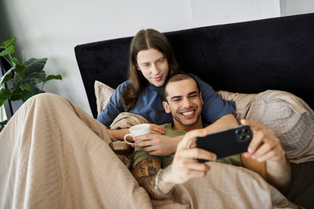 Two young men, snuggled in bed, share a warm smile and a cozy morning.の写真素材