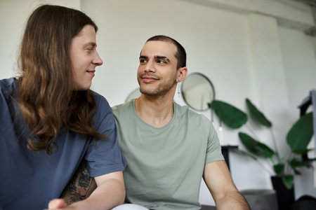 A young gay couple shares a quiet moment of intimacy in their bedroom, their eyes locked in a loving gaze.の写真素材