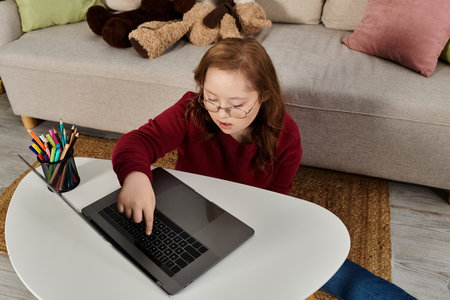A little girl with Down syndrome sits on the floor at home, using a laptop.