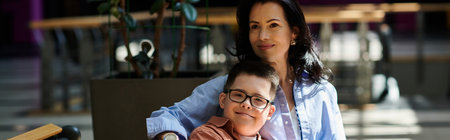 A mother and her son with Down syndrome are seen walking together in a shopping mall, enjoying each...