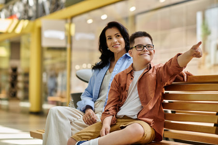 A mother and her son with Down syndrome share a moment of joy and laughter while sitting on a bench in a shopping mall.の写真素材