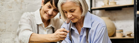 A mature lesbian couple, dressed in cozy attire, works on a pottery project in an art studio.