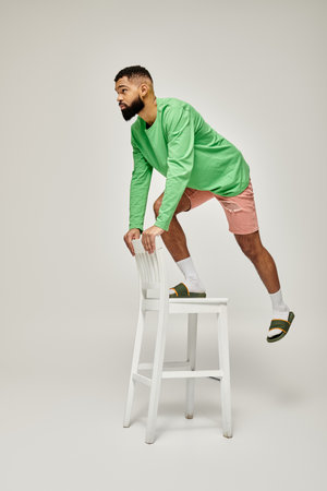 African American man in green shirt standing on stool against vibrant backdrop.