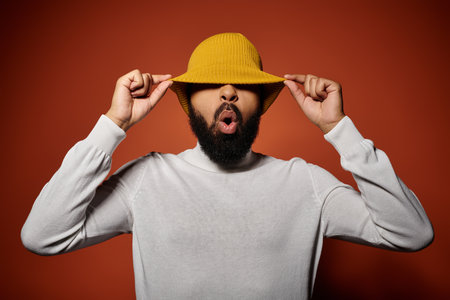 A handsome African American man in fashionable attire poses with a funny face on a vibrant backdrop.の写真素材