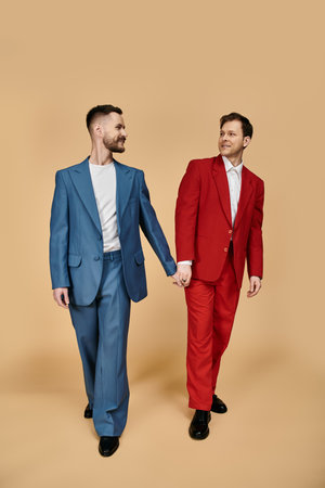 Two men in elegant suits walk hand-in-hand, showcasing a vibrant blue and red color combination.