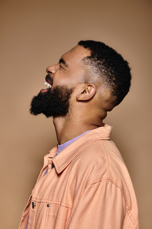 African American man with beard in pink shirt poses against colorful background.