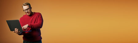 Handsome man in a red sweater actively using a laptop computer.の写真素材