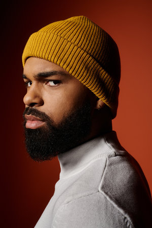 Handsome man with beard in trendy outfit and yellow hat against colorful backdrop.