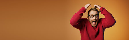 Handsome man in red sweater holding head with hands.