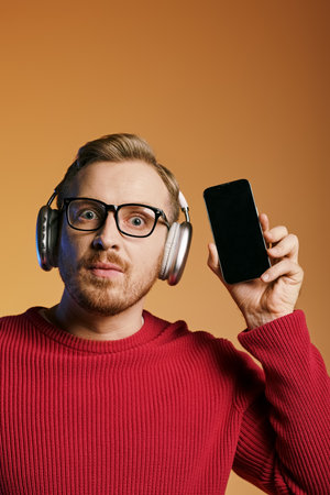 Stylish man in headphones holding cellphone, immersed in music.