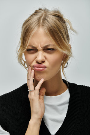 A stylish young blonde woman making a face against a grey background.