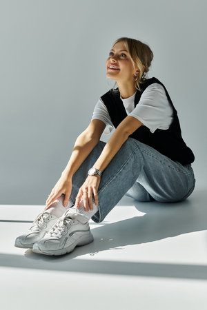 A young blonde woman sits on the ground, holding a pair of sneakers, exuding a sense of peaceful...