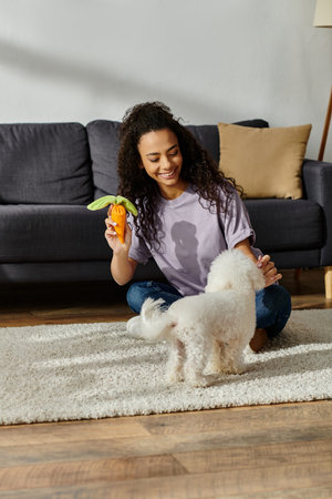 A young woman delightedly interacts with her fluffy Bichon Frise dog on the floor.