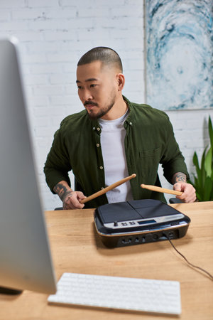 An Asian man with a beard, wearing a green shirt, plays drums in a studio setting.