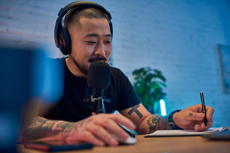 A handsome Asian man wearing headphones speaks into a microphone in his podcast studio.の写真素材