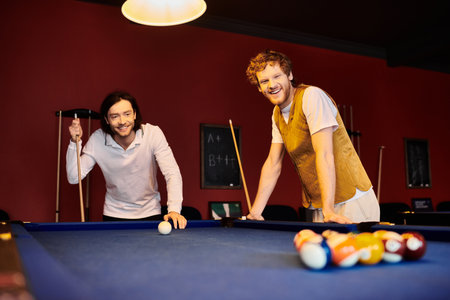 Two men in casual clothing play pool together in a dimly lit room.の写真素材