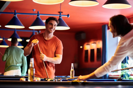 Friends enjoy a casual game of billiards in a bar with a vibrant red wall and blue lights.の写真素材