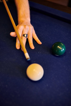 A hand holding a pool cue, aiming at a white ball on a green felt pool table.