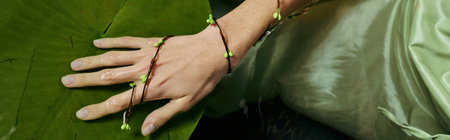 A womans hand with green floral jewelry rests on a large green leaf near a swamp.の写真素材