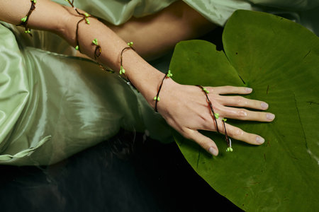 A womans hand adorned with a delicate green bracelet rests on a large lily pad.の写真素材