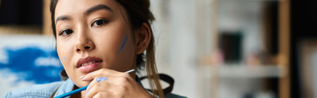 A young Asian woman artist in a workshop, wearing an apron and painting.の写真素材