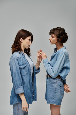 Two young women in denim shirts and jeans pose against a grey background.の写真素材