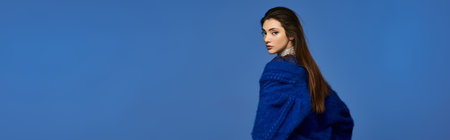 A young woman in a blue sweater stands against a blue background.の写真素材