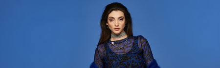 A young woman in a blue dress stands against a solid blue backdrop.