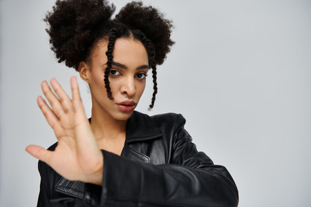 A young African American woman in a black leather jacket poses against a grey background.の写真素材
