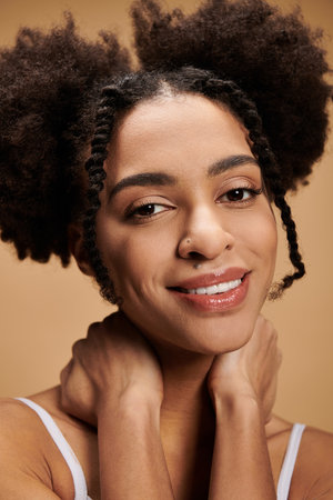 A young Black woman with a warm smile and a beautiful hairstyle looks directly at the camera against a beige backdrop.の写真素材