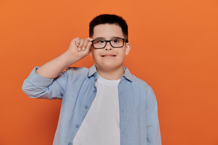 A young boy with Down syndrome looks confidently at the camera while adjusting his glasses.の写真素材
