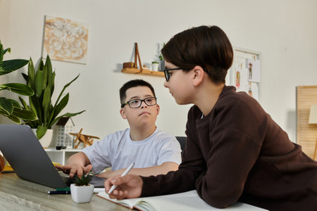Two young boys work together at home, one using a laptop and the other writing in a notebook.