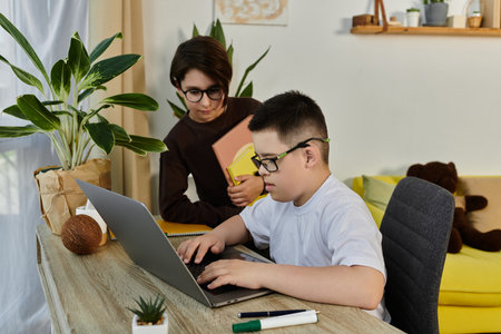 A young boy with Down syndrome sits at a desk with a friend, using a laptop.の写真素材