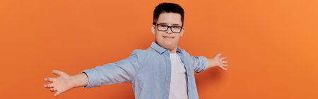 Young boy with Down syndrome happily hugs, orange backdrop.