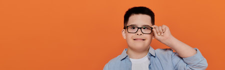 A young boy with Down syndrome poses confidently against an orange background.