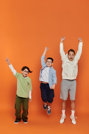 Three young boys, including one with Down syndrome, jump for joy in front of an orange backdrop.